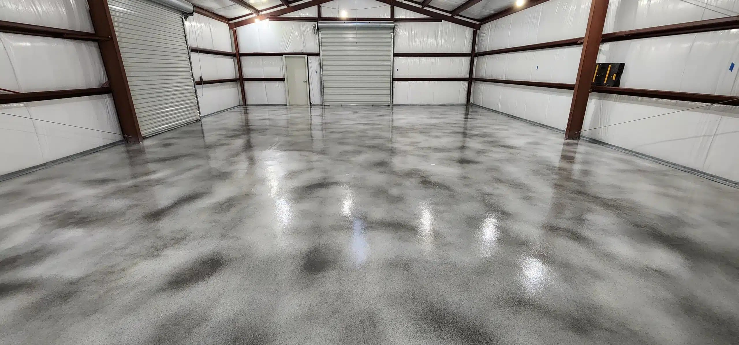 Gray metallic epoxy floor in a metal building, freshly finished, painter's tape still on the wall